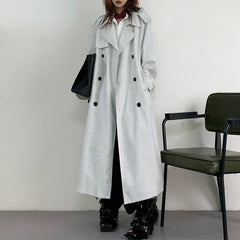 Person wearing a long black and white striped coat in a minimalistic setting with a chair.