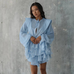 Woman wearing a light blue ruffled dress against a gray concrete wall