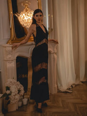 Woman in a black dress standing in an elegant room with a chandelier and fireplace.
