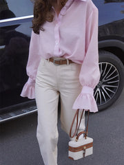 Person wearing a pink blouse and white pants holding a small handbag, standing next to a car.