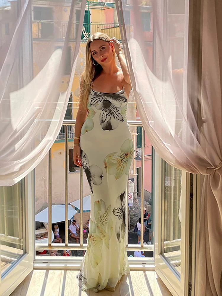 Woman in a floral dress standing in front of a window with white curtains.