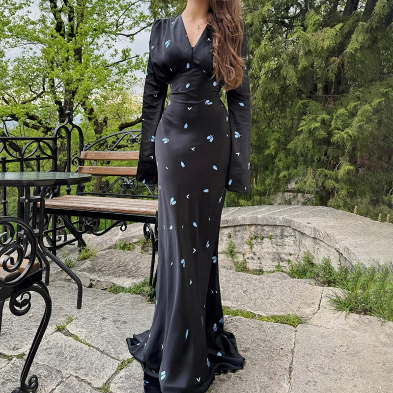 Woman in a black dress with blue patterns standing outdoors in a park-like setting.