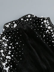 Black off-shoulder top with pearl embellishments on a gray background