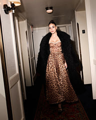 Woman wearing a leopard print dress and black coat in a hallway.