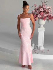 Woman in a pink evening gown standing next to a floral arrangement in a decorative setting.