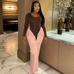 Woman in a brown top and pink pants standing in an indoor setting with decorative elements.