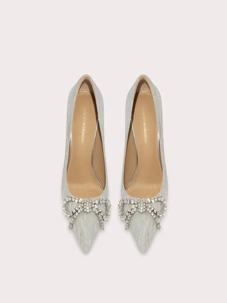Pair of silver pointed-toe shoes with embellishments on a light gray background