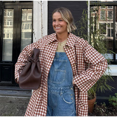 Woman wearing a red and white checkered coat over denim overalls, standing outdoors.