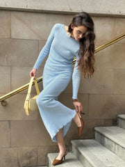 Woman in a light blue dress standing on steps with a beige wall background