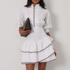 White dress with black trim worn by a person on a plain background