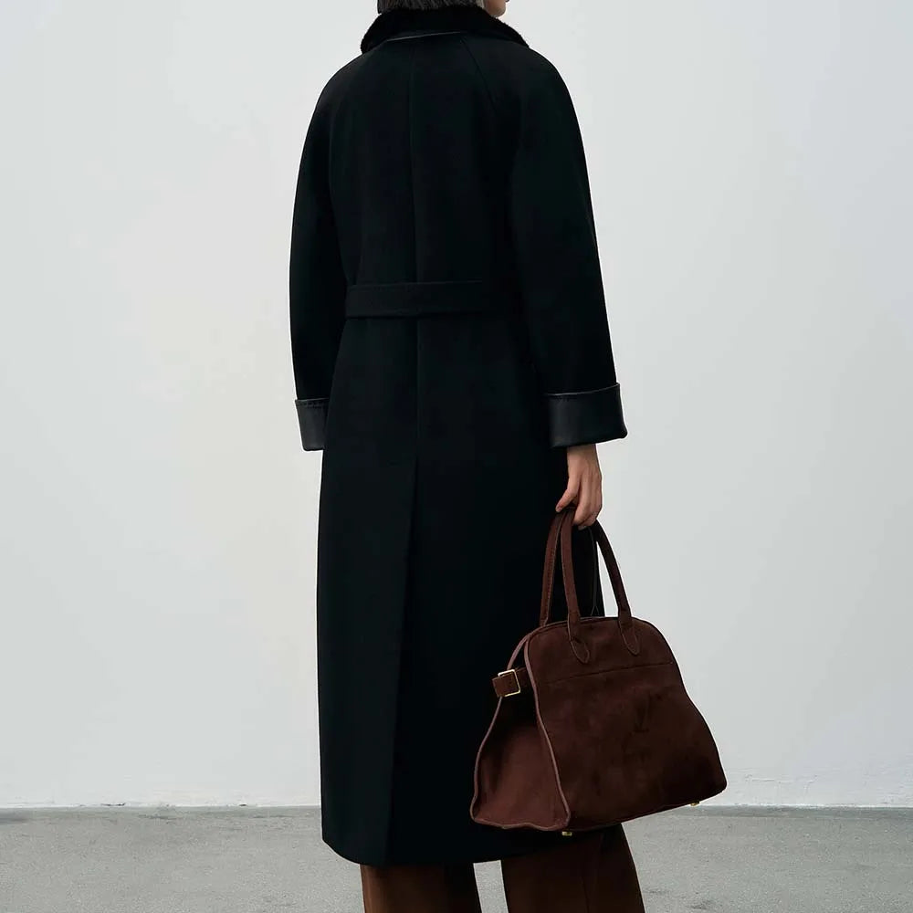 Person wearing a black coat holding a brown bag against a white background