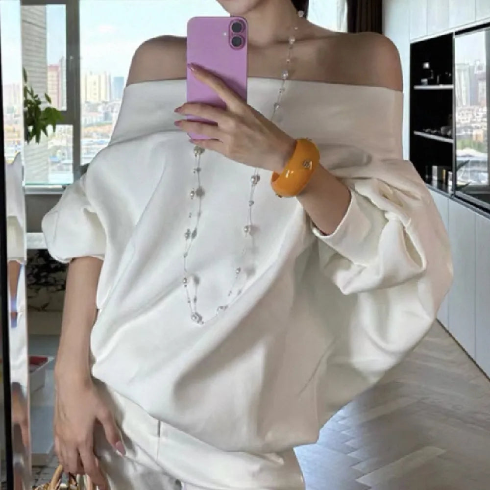 Person wearing a white off-shoulder top with pearl details, holding a pink phone.