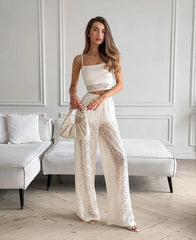 Woman in a white lace outfit holding a matching handbag in a minimalistic room.