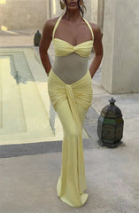 Woman wearing a yellow two-piece swimsuit with a draped skirt in an outdoor setting.