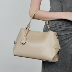 Beige handbag held by a person wearing a gray dress on a light gray background