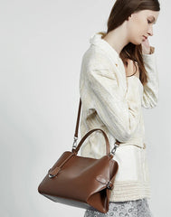 Woman holding a brown leather handbag against a plain background