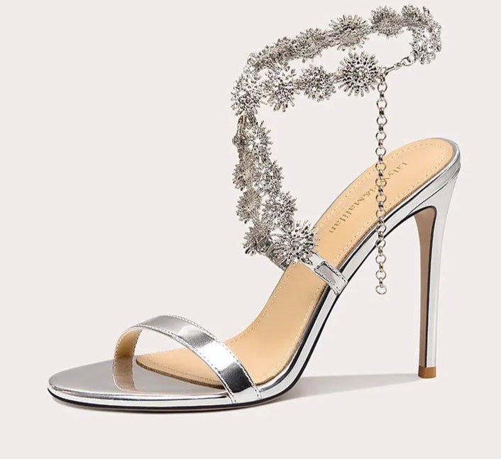 Silver high-heeled sandal with decorative chain on a white background