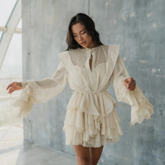 Woman wearing a white dress with ruffled sleeves and layers in a minimalistic setting.