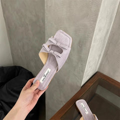 Gray suede sandal held by a hand against a neutral background