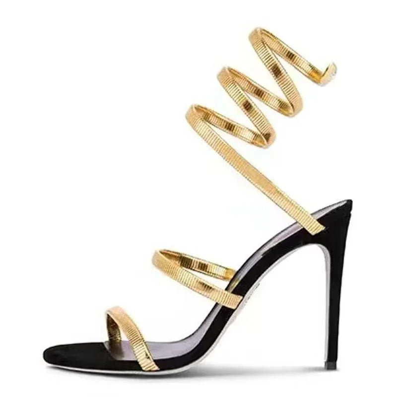 Black high-heeled sandal with gold spiral straps on a white background