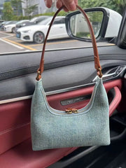 Green handbag with brown handle held by a person inside a car.