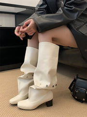 Person wearing white knee-high boots sitting on a couch with a black handbag beside them.