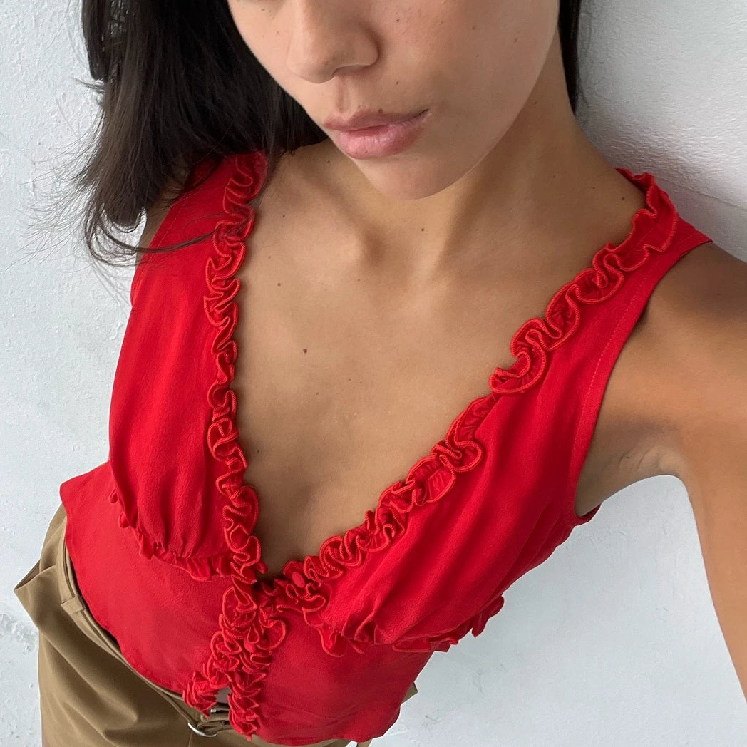 Red ruffled V-neck tank top worn by a woman against a white wall background