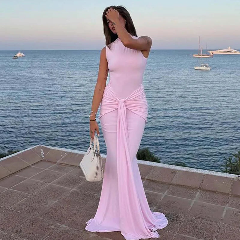 Woman in a pink dress standing by the sea with boats in the background