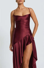 Woman wearing a burgundy satin dress with a slit on a light gray background