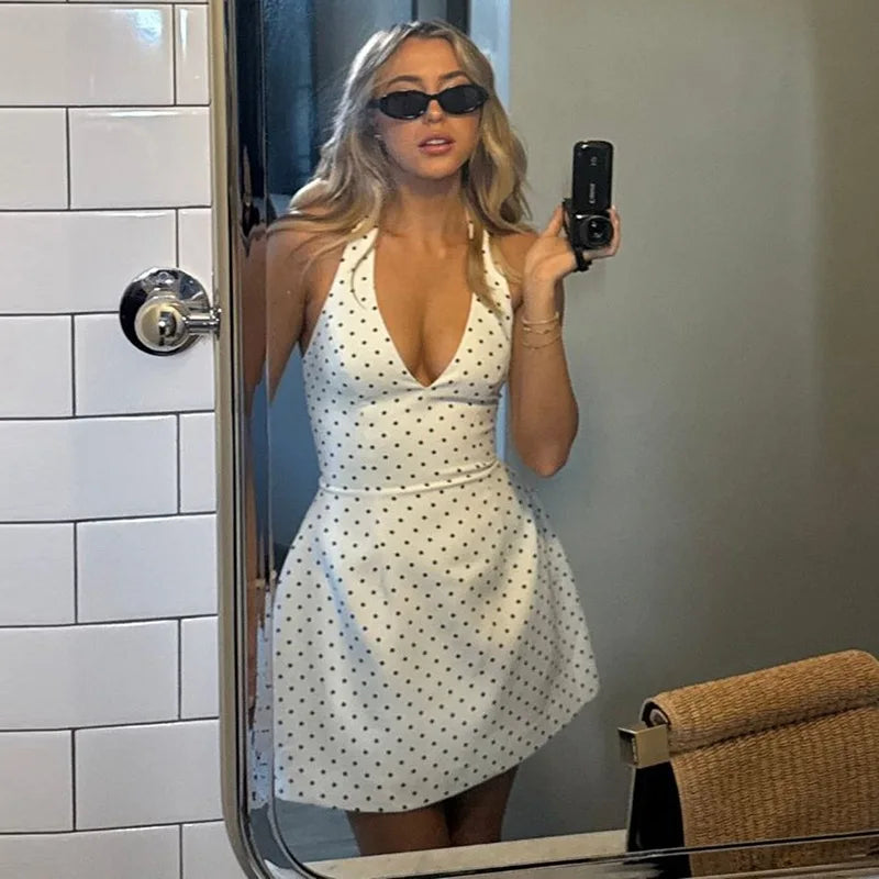 Woman taking a mirror selfie wearing a white polka dot dress in a bathroom.