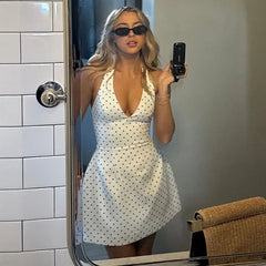 Woman taking a mirror selfie wearing a white polka dot dress in a bathroom.