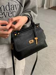 Person holding a black handbag with a gold lock on a light gray floor.