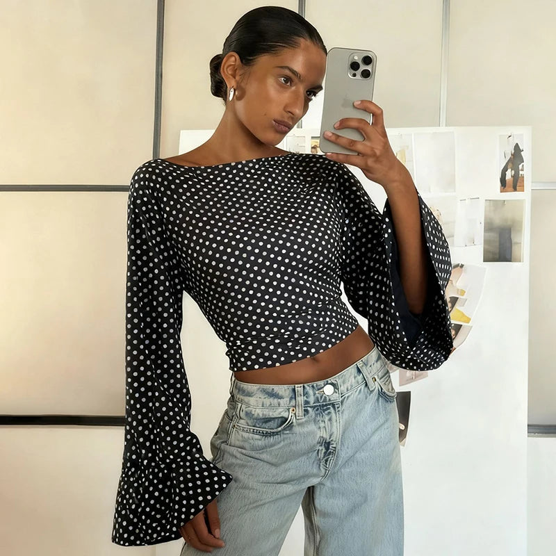 Woman taking a mirror selfie wearing a black polka dot top and light blue jeans.
