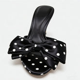 Black sandal with a large bow featuring white polka dots on a light gray background
