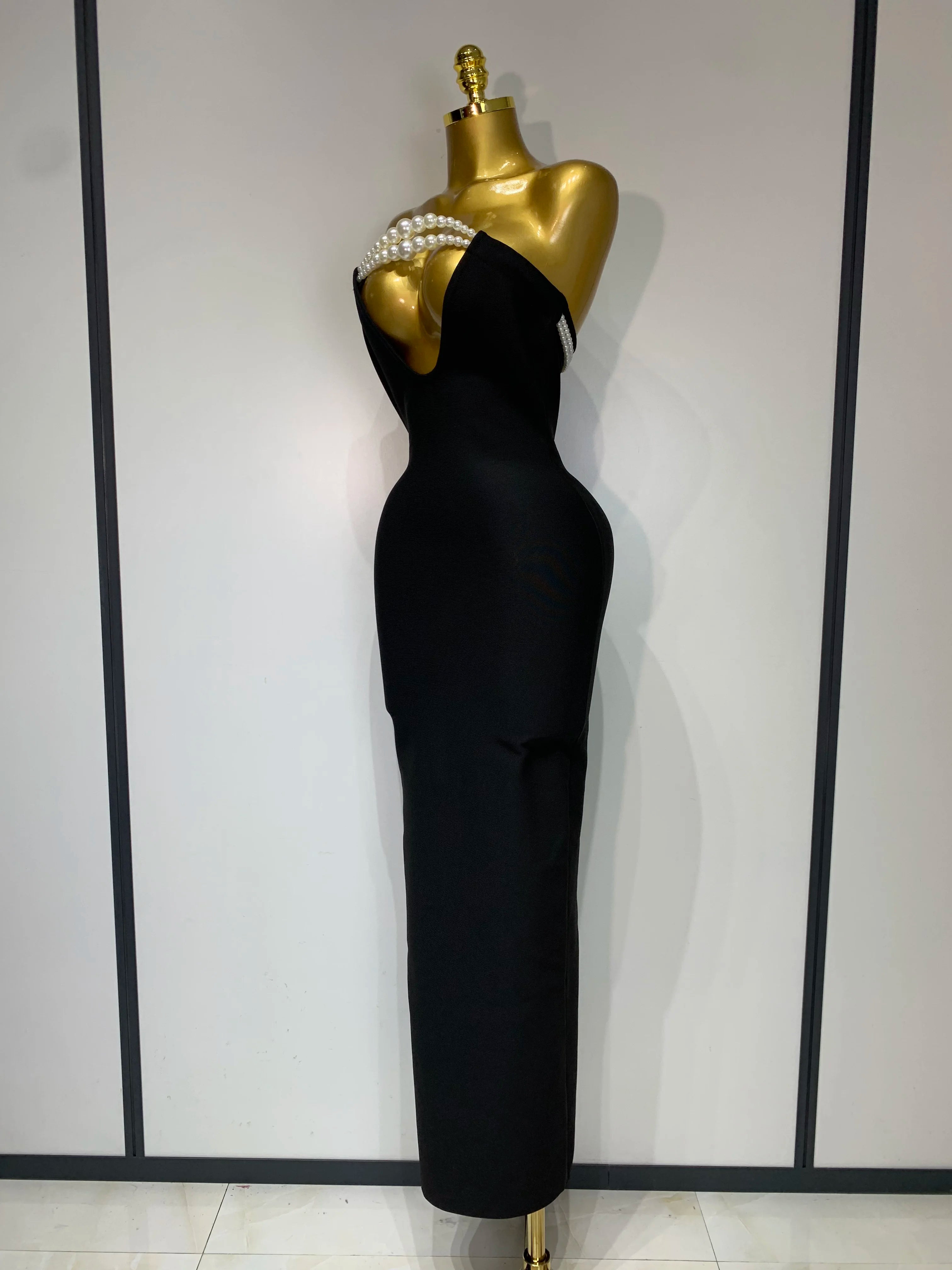 Black evening gown on a mannequin against a white wall with black vertical stripes.