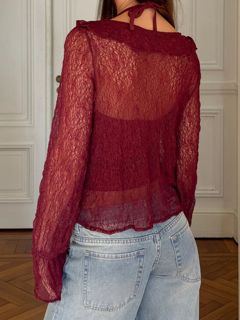 Red lace top worn by a person with light blue jeans in an indoor setting.
