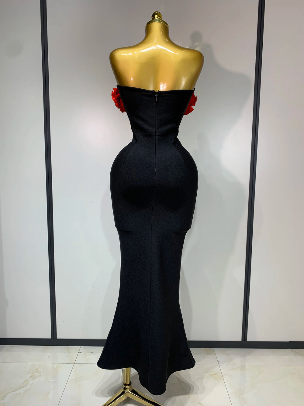 Black evening gown on a mannequin against a white wall.