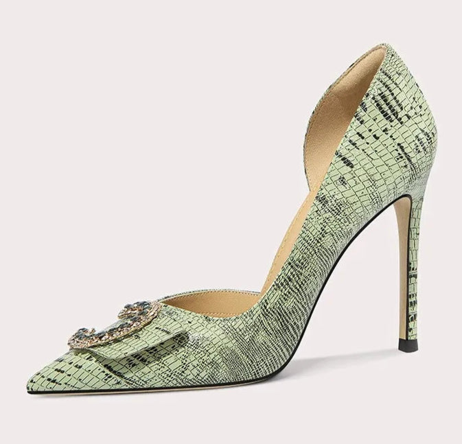 Green high-heeled shoe with a decorative brooch on a light gray background