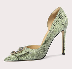 Green high-heeled shoe with a decorative brooch on a light gray background