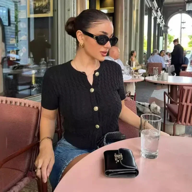 Woman sitting at a table in an outdoor cafe wearing sunglasses and a black top.