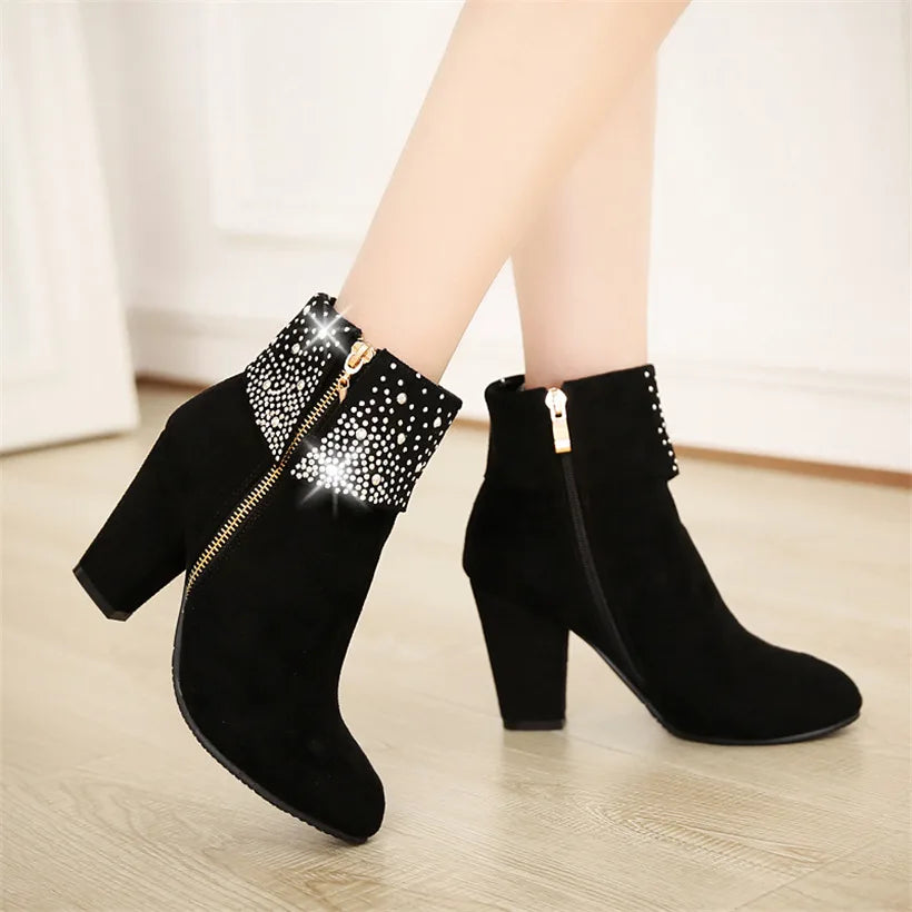 Black ankle boots with rhinestone details on a light wooden floor.