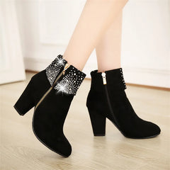 Black ankle boots with rhinestone details on a light wooden floor.