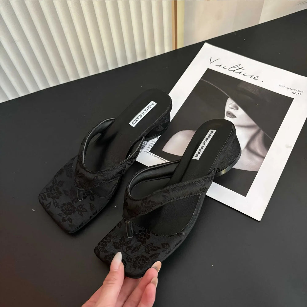 Black floral-patterned sandals on a black surface with a magazine underneath