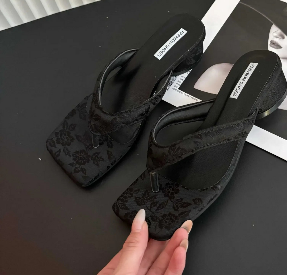 Black floral-patterned sandals on a black surface with a magazine underneath