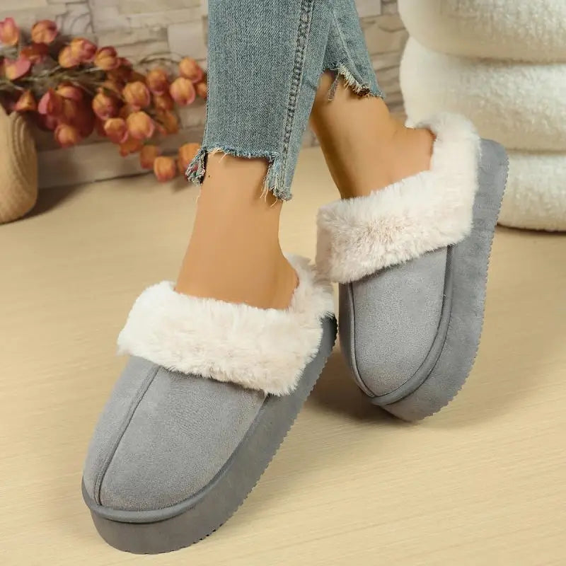 Gray slippers with white fur trim worn by a person on a beige surface.