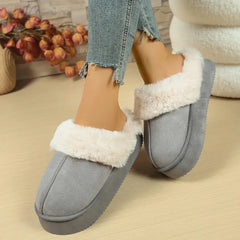 Gray slippers with white fur trim worn by a person on a beige surface.