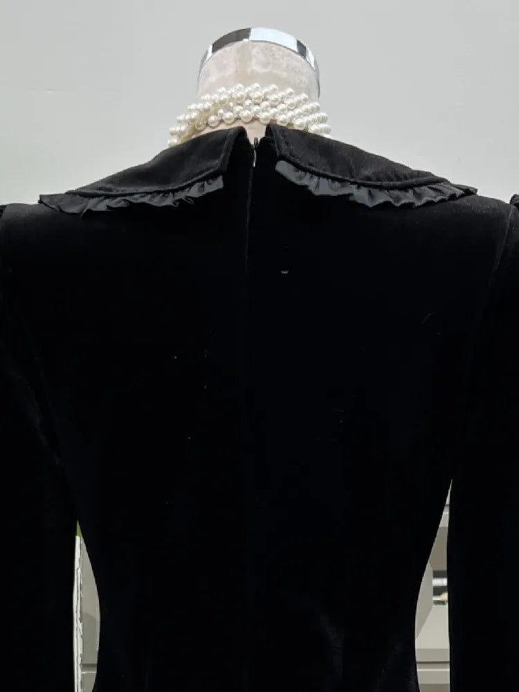 Black velvet garment with a large ruffled collar on a mannequin against a neutral background