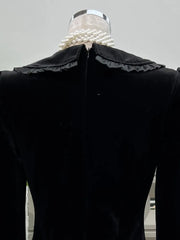 Black velvet garment with a large ruffled collar on a mannequin against a neutral background