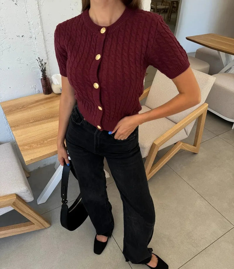 Person wearing a maroon cable knit cardigan with gold buttons in an indoor setting.