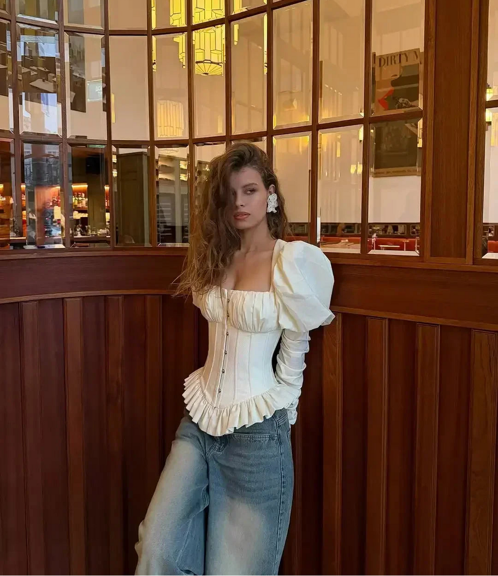 Woman in a white top and jeans standing in a decorative interior setting.
